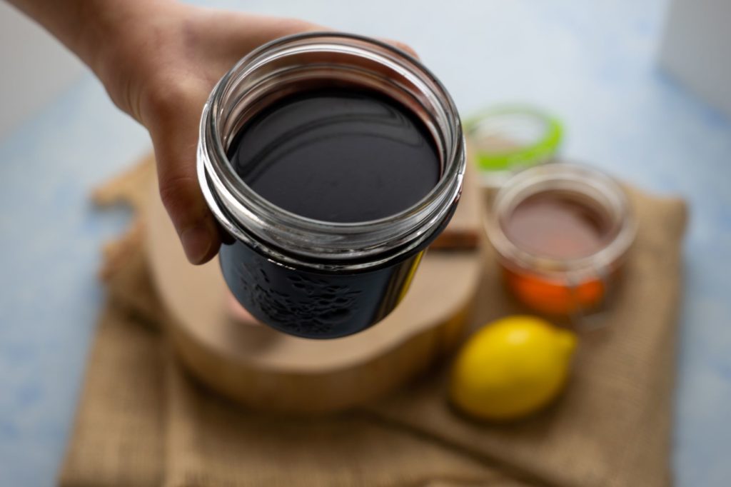 A mason jar cup of elderberry syrup held by hand 